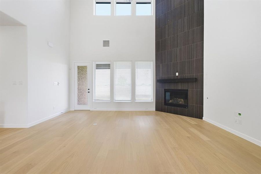 High-ceiling room featuring light wood-finish flooring and a contemporary fireplace with a dark tile surround and integrated mantle