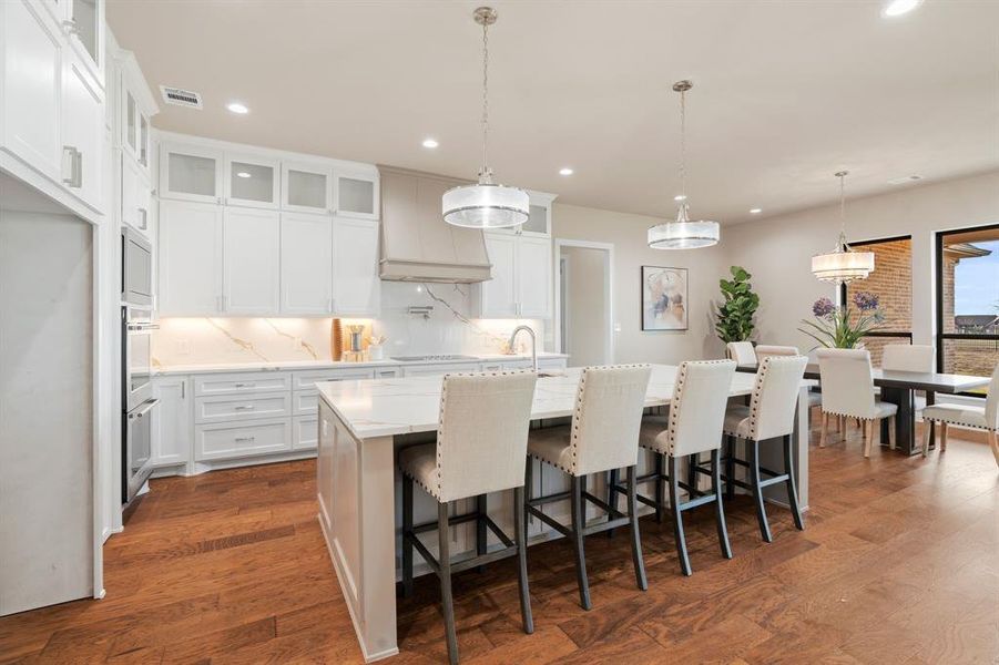 Kitchen featuring decorative light fixtures, white cabinetry, backsplash, premium range hood, and a kitchen island with sink