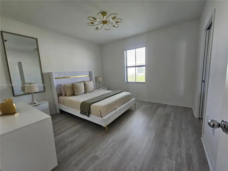 Bedroom featuring wood-finish flooring, a multi-arm metallic ceiling fixture, and a single-pane window with installed blinds