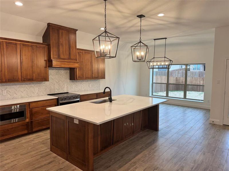 Kitchen featuring appliances with stainless steel finishes, tasteful backsplash, sink, hanging light fixtures, and a center island with sink
