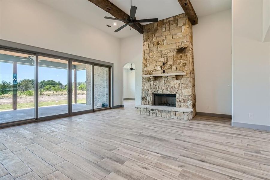 Unfurnished living room featuring a fireplace, light hardwood / wood-style flooring, ceiling fan, and beam ceiling