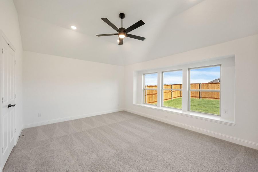 Empty bedroom with gray carpet, ceiling fan, and triple window overlooking fenced backyard Empty bedroom with gray carpet, ceiling fan, and triple window overlooking fenced backyard