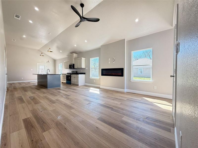 Unfurnished living room featuring ceiling fan, light wood-style floors, lofted ceiling, a glass covered fireplace, and recessed lighting