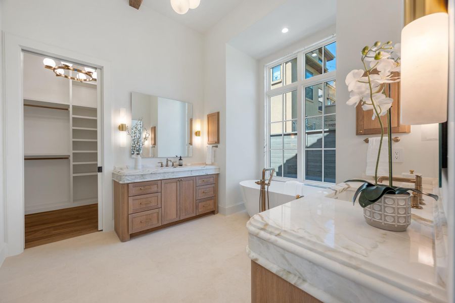 High ceilings and stone counters elevate this primary bathroom featuring a freestanding soaking tub.