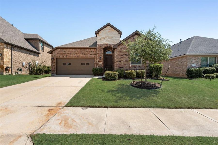 French country inspired facade featuring brick siding, driveway, a front yard, an attached garage, and a shingled roof French country inspired facade featuring brick siding, driveway, a front yard, an attached garage, and a shingled roof