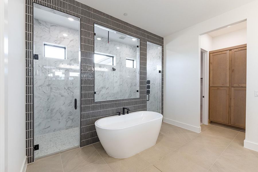 Primary bath with a marble finish shower, a freestanding bath, and light tile patterned flooring