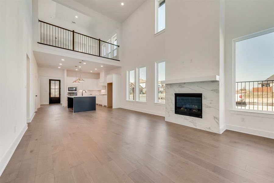 Unfurnished living room featuring light wood finished floors, a fireplace, recessed lighting, and a towering ceiling Unfurnished living room featuring light wood finished floors, a fireplace, recessed lighting, and a towering ceiling