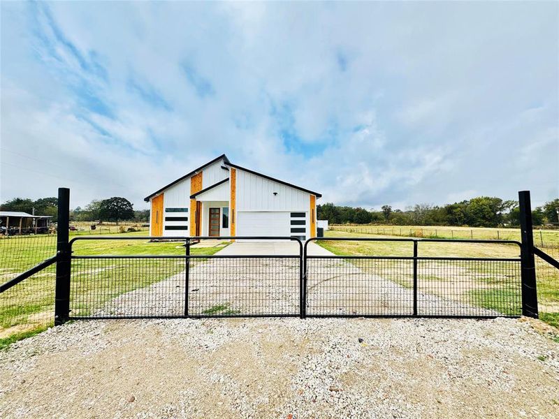 View of front of home featuring a gate, a garage, driveway, and a view of rural / pastoral area View of front of home featuring a gate, a garage, driveway, and a view of rural / pastoral area