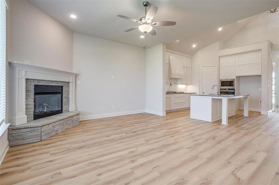 Unfurnished living room featuring sink, a fireplace, light wood-type flooring, high vaulted ceiling, and ceiling fan