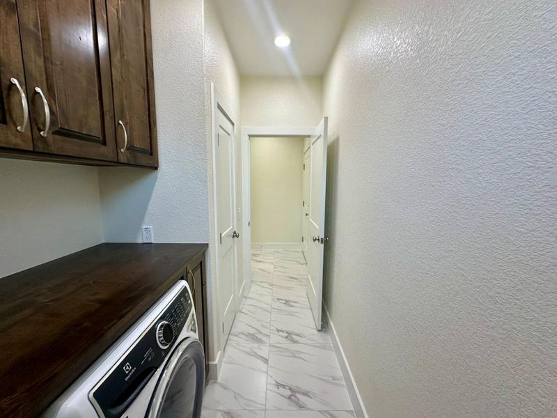 Laundry area featuring light marble finish flooring, a textured wall, washer / clothes dryer, and cabinet space