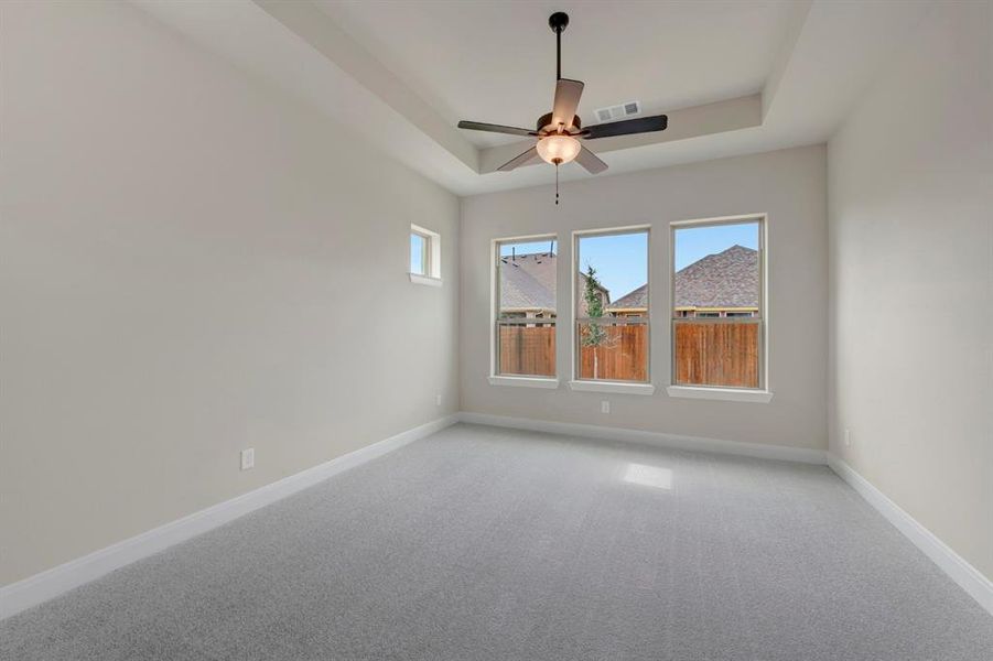Empty room with light carpet, ceiling fan, and a tray ceiling