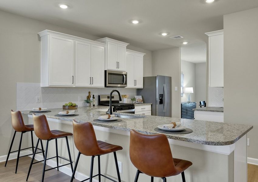 Kitchen island with a granite countertop, leather bar stools, white cabinetry, and stainless appliances.