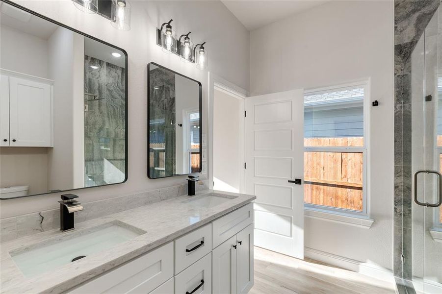Main bathroom featuring double vanity, light wood finished floors, and a shower stall