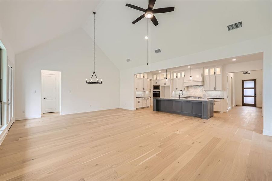 Unfurnished living room featuring high vaulted ceiling, sink, light wood-type flooring, and ceiling fan with notable chandelier