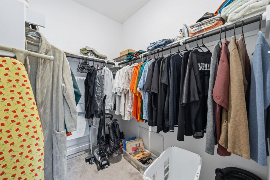 Walk-in closet featuring white walls, grey carpet flooring, and a multi-tiered closet organization system with both upper shelving and hanging rods