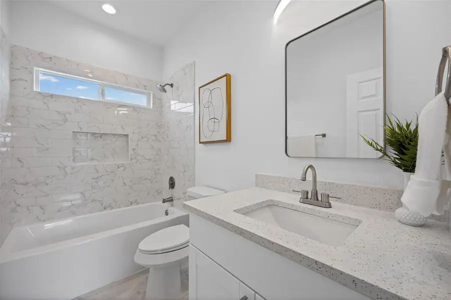 A well-lit bathroom features a vanity with stone counters and a tub with tiled walls, all set under a convenient transom window. A well-lit bathroom features a vanity with stone counters and a tub with tiled walls, all set under a convenient transom window.