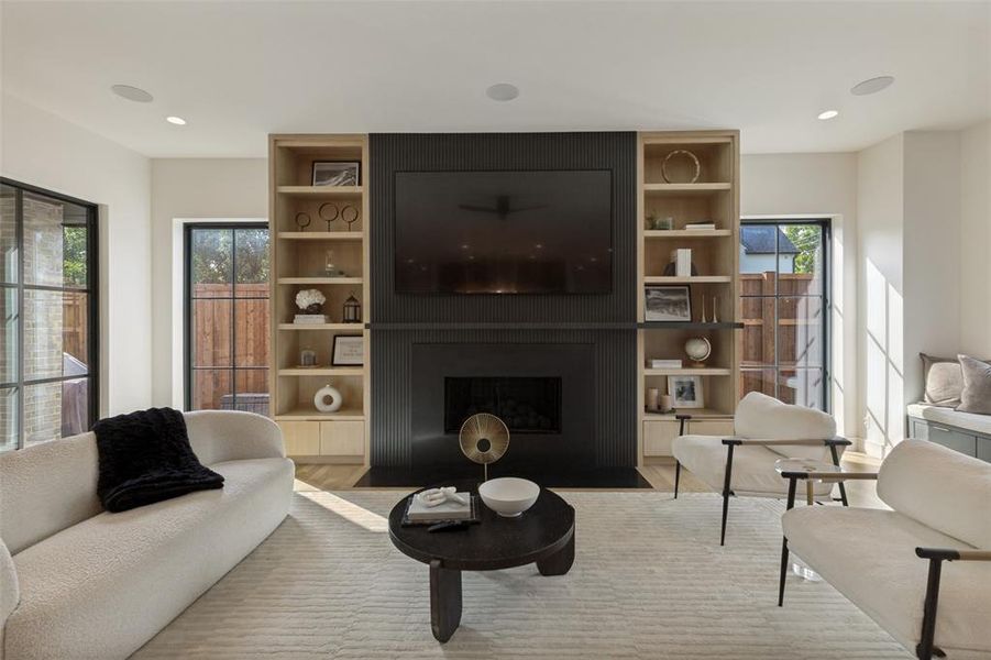 Living area featuring a modern fireplace with a black paneled surround, flanked by built-in light wood shelving with integrated cabinetry Living area featuring a modern fireplace with a black paneled surround, flanked by built-in light wood shelving with integrated cabinetry