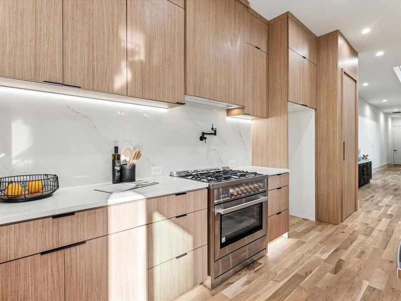 Kitchen featuring tasteful backsplash, stainless steel range, light hardwood / wood-style flooring, and light brown cabinets