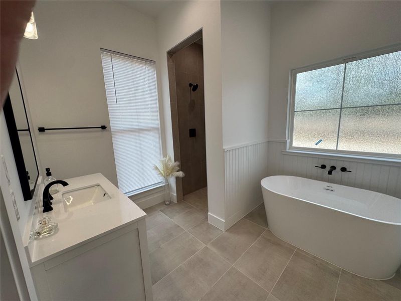 Full bathroom featuring vanity, a walk in shower, a freestanding bath, wainscoting, and light tile patterned floors Full bathroom featuring vanity, a walk in shower, a freestanding bath, wainscoting, and light tile patterned floors