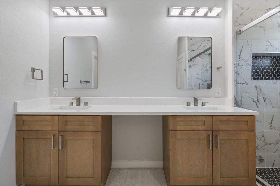 A well-lit primary bathroom featuring dual vanities, modern fixtures, and a glass-enclosed shower with stylish tile work.