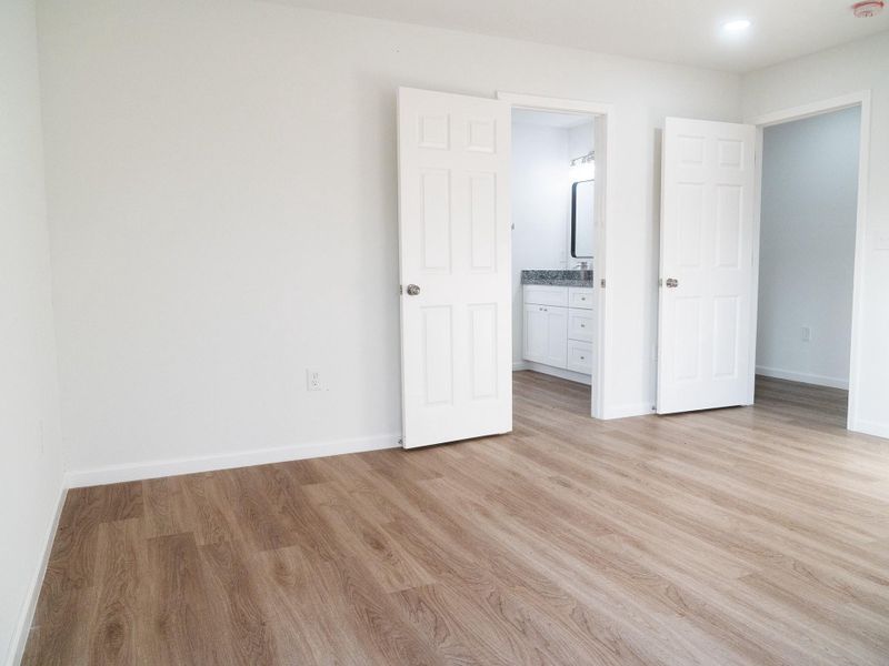 This photo showcases a bright, spacious bedroom with light wood flooring and white walls. It features an en-suite bathroom with modern fixtures and ample natural light.