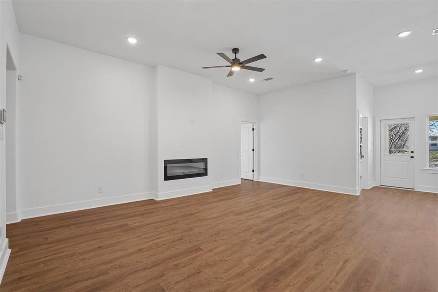 Unfurnished living room with wood finished floors, baseboards, recessed lighting, ceiling fan, and a glass covered fireplace