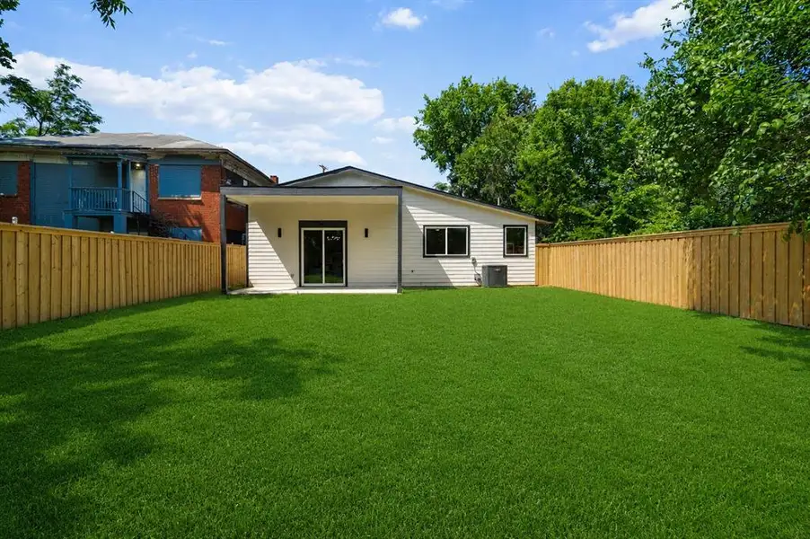 Expansive backyard featuring a manicured lawn, a newly installed wood privacy fence, and a modern exterior with sliding glass doors Expansive backyard featuring a manicured lawn, a newly installed wood privacy fence, and a modern exterior with sliding glass doors