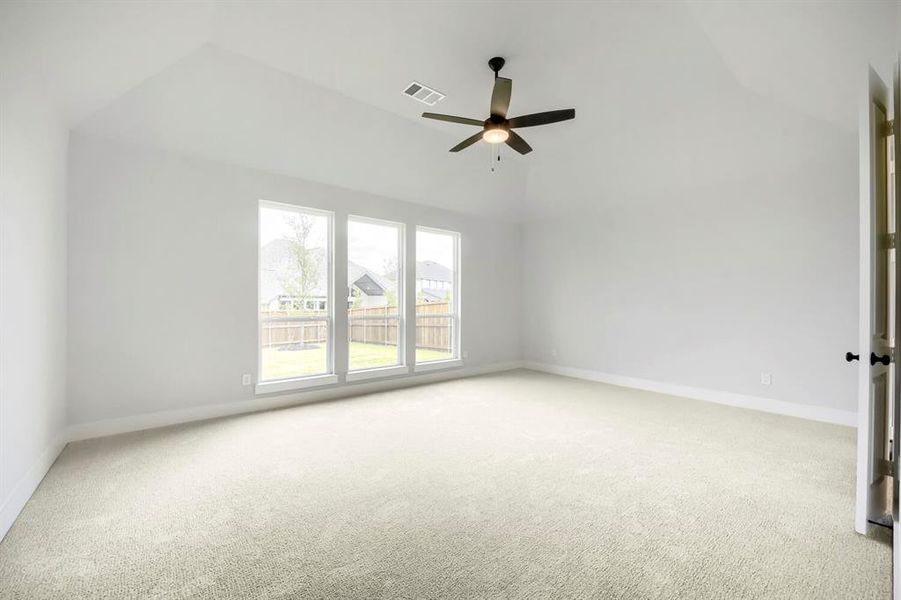 Spacious room featuring vaulted ceilings, light-colored carpeting, three large windows, a ceiling fan with integrated lighting, and a neutral wall palette