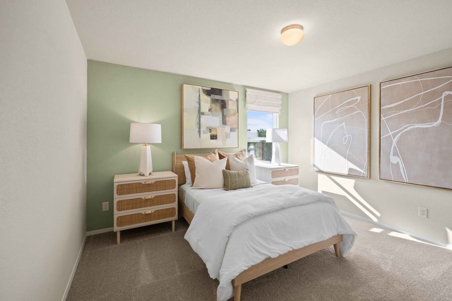 An interior image of a bedroom with a green painted wall, brown carpet, wall art, and a bed with white bedding.