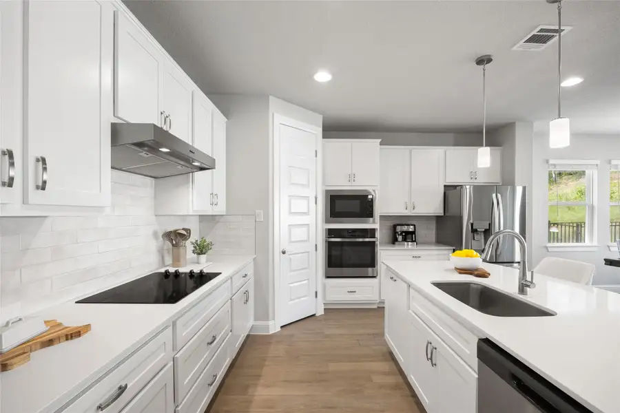 The kitchen features stainless steel appliances, light wood-style flooring, crisp white cabinetry, recessed lighting, and an abundance of natural light—creating a bright and inviting space for cooking and gathering.