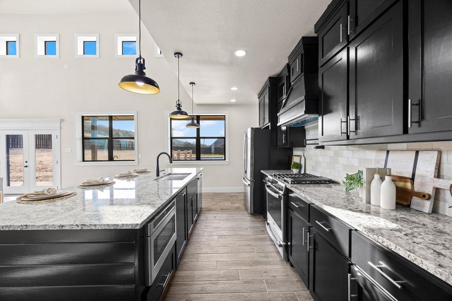 Kitchen with dark cabinetry, light stone countertops, stainless steel appliances, hanging light fixtures, and recessed lighting Kitchen with dark cabinetry, light stone countertops, stainless steel appliances, hanging light fixtures, and recessed lighting