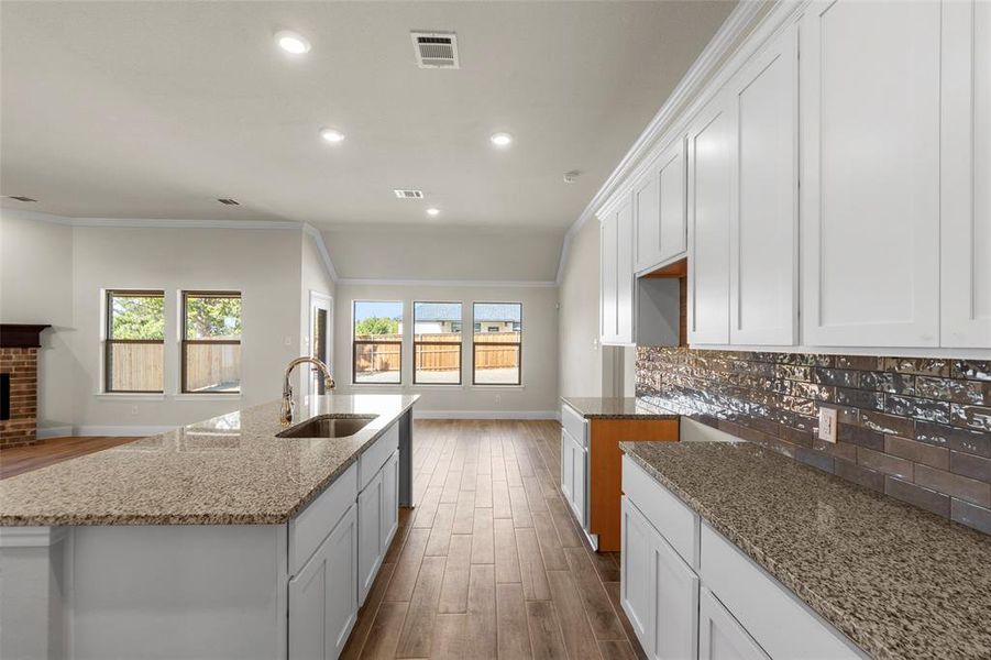 Kitchen with white cabinetry, dark wood-type flooring, light stone countertops, a center island with sink, and recessed lighting