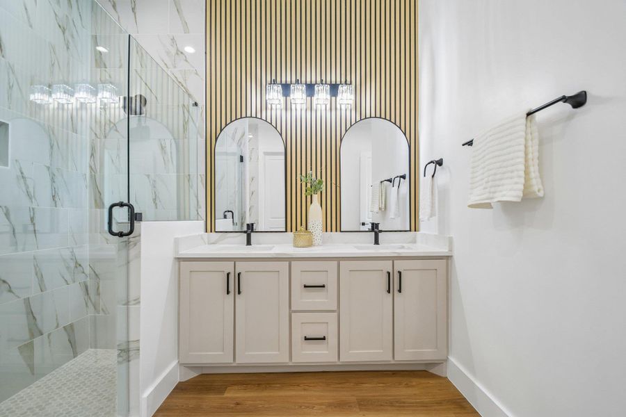 Double vanities sit beneath arched mirrors and wood-paneled walls adjacent to a glass shower. Double vanities sit beneath arched mirrors and wood-paneled walls adjacent to a glass shower.