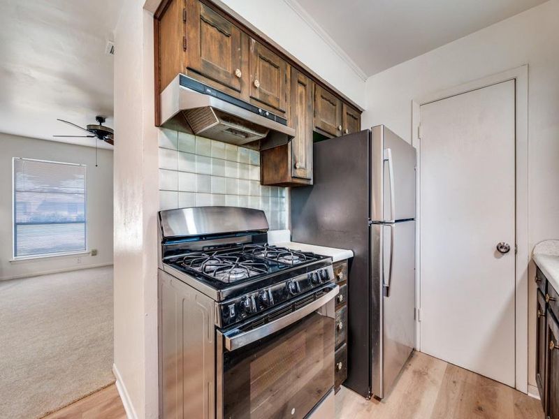 Kitchen with stainless steel gas range, under cabinet range hood, light wood finished floors, light countertops, and tasteful backsplash Kitchen with stainless steel gas range, under cabinet range hood, light wood finished floors, light countertops, and tasteful backsplash