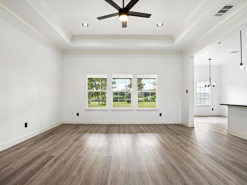 Unfurnished living room with a raised ceiling, ceiling fan with notable chandelier, ornamental molding, and hardwood / wood-style flooring