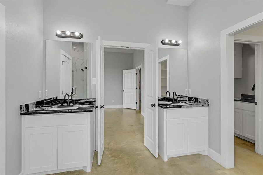 Full bathroom featuring a shower stall, two vanities, finished concrete flooring, and baseboards