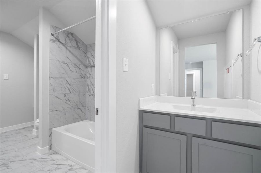 This secondary jack-n-jill bath features tile flooring, bath/shower combo with tile surround, stained wood cabinets, beautiful light countertops, mirror, sleek fixtures and modern finishes.