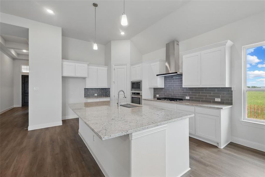Kitchen featuring wall chimney range hood, a center island with sink, stainless steel appliances, white cabinetry, and dark wood-type flooring