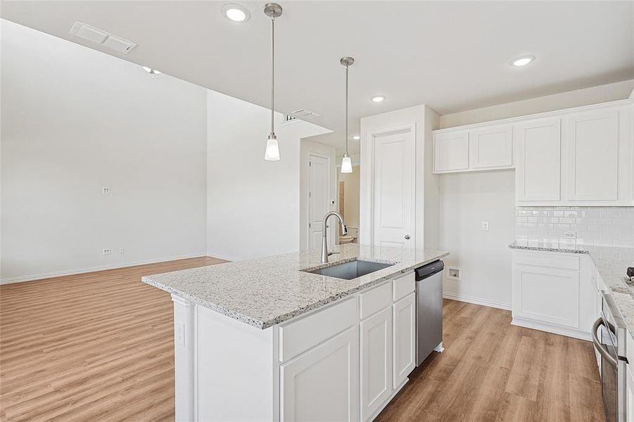 Kitchen featuring white cabinets, light stone countertops, an island with sink, light wood-type flooring, and hanging light fixtures