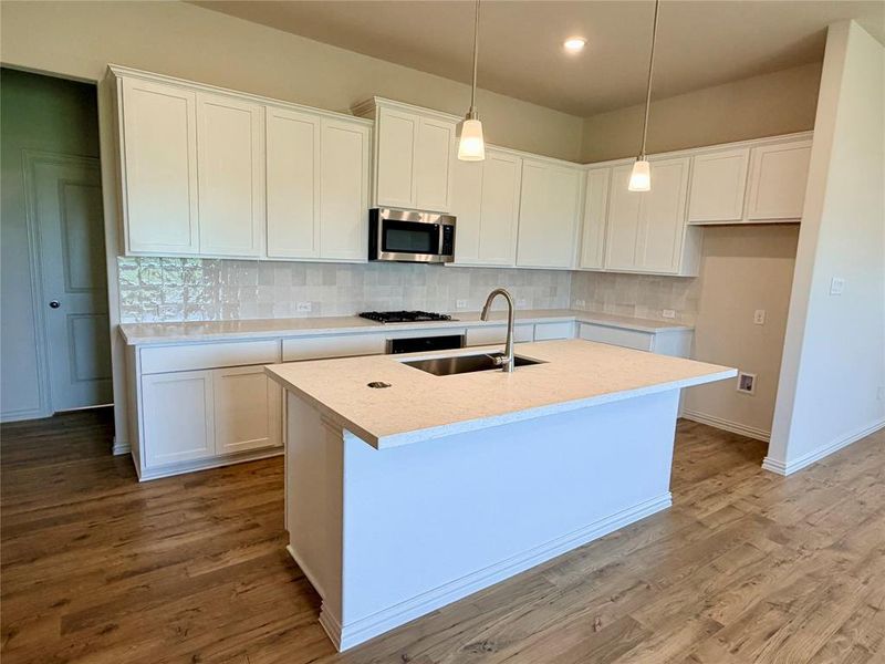 Spacious kitchen featuring white cabinetry, light-toned countertops, a tile backsplash, and wood-finish flooring