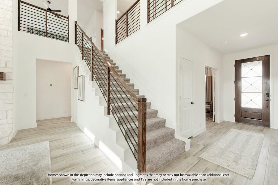 Two-story foyer with carpeted staircase, metal railing, light wood floors, and glass-panel front door