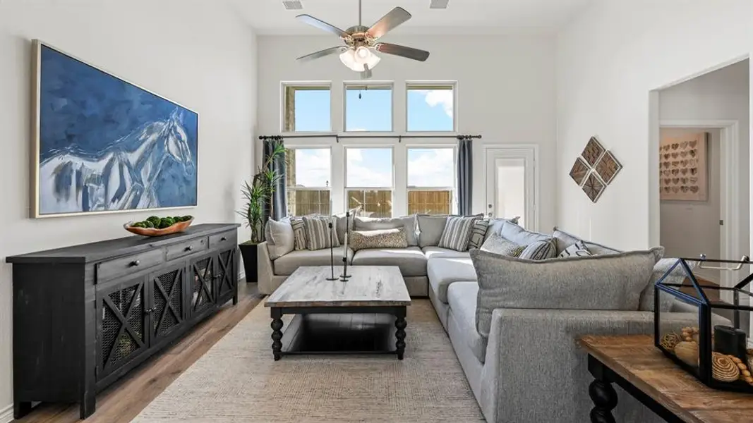 Living area featuring a vaulted ceiling with a ceiling fan, wood-finish flooring, and a bank of windows