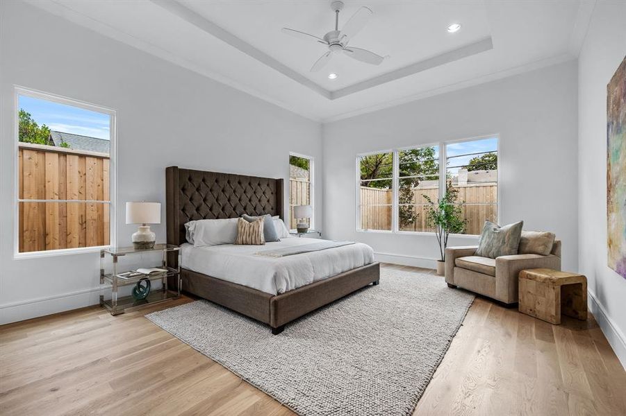 Bedroom with ceiling fan, light hardwood / wood-style floors, and a tray ceiling