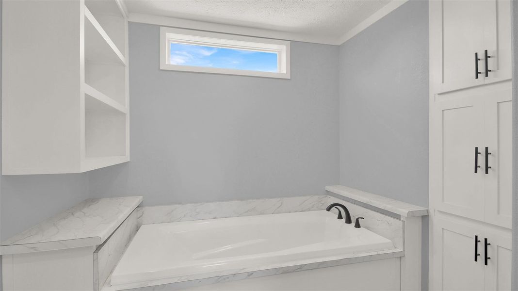 Built-in cabinetry and stone surfaces flank a deep soaking tub beneath a clerestory window.