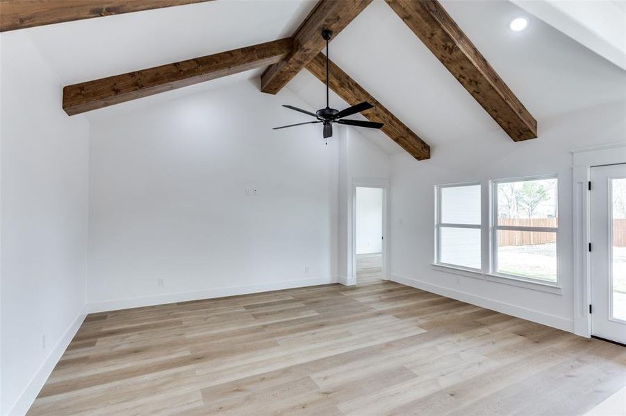 Empty room with high vaulted ceiling, light wood finished floors, beam ceiling, and baseboards