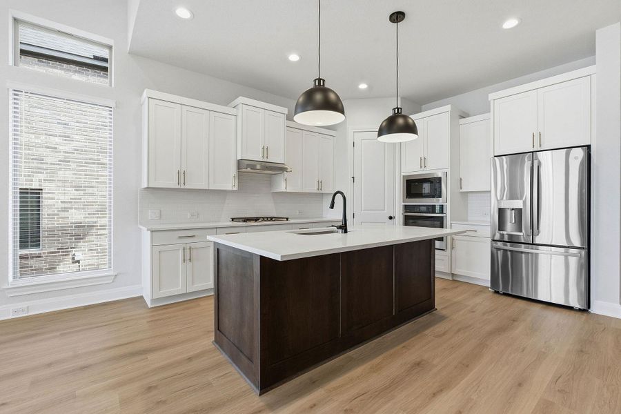 Dual tone kitchen with stainless steel appliances, dual tone cabinetry, hanging light fixtures, a center island with sink, and light wood-type flooring
