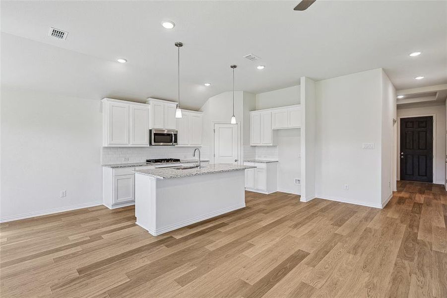 Kitchen with a center island with sink, light hardwood / wood-style flooring, stainless steel appliances, decorative backsplash, and white cabinetry