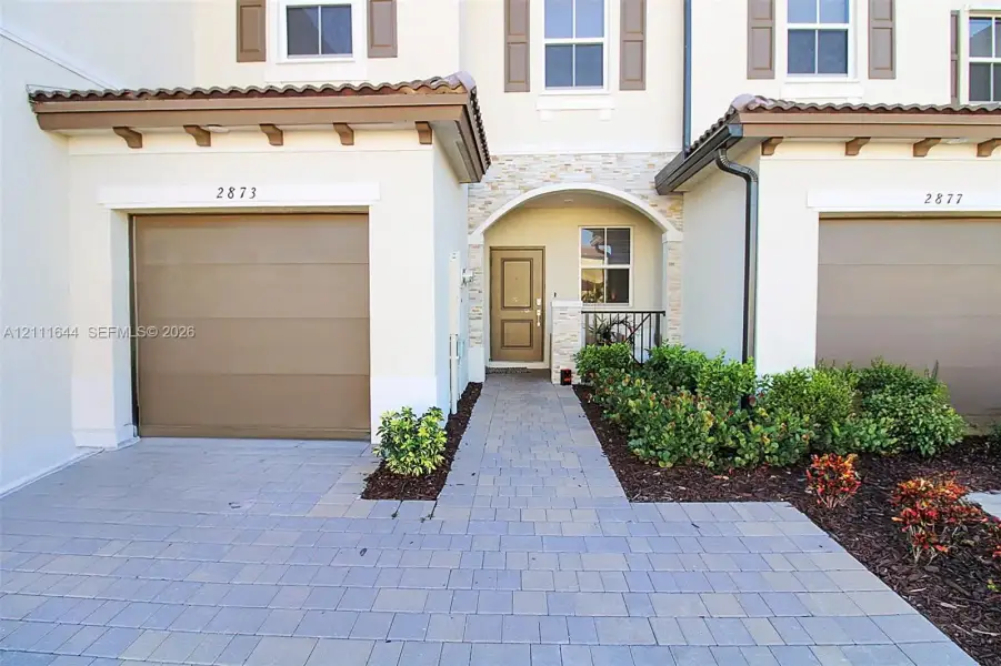Exterior featuring a paver driveway, single-car garage, stone veneer entryway accents, and a covered portico with arched detailing Exterior featuring a paver driveway, single-car garage, stone veneer entryway accents, and a covered portico with arched detailing