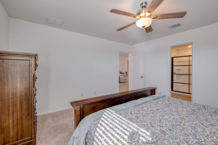 This bedroom features light-colored walls, carpeted flooring, and a ceiling fan with light fixture