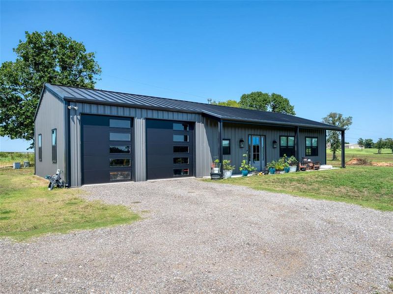 View of front of home featuring board and batten siding, a front lawn, a metal roof, a porch, and gravel driveway View of front of home featuring board and batten siding, a front lawn, a metal roof, a porch, and gravel driveway